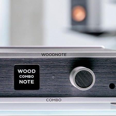 Lindemann Woodnote COMBO streaming amplifier on a glass shelf, loudspeaker softly out of focus behind it