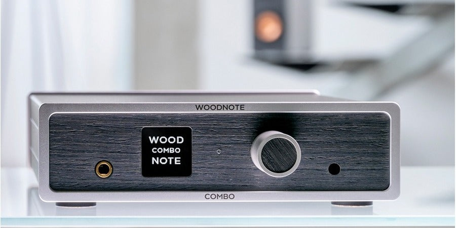 Lindemann Woodnote COMBO streaming amplifier on a glass shelf, loudspeaker softly out of focus behind it